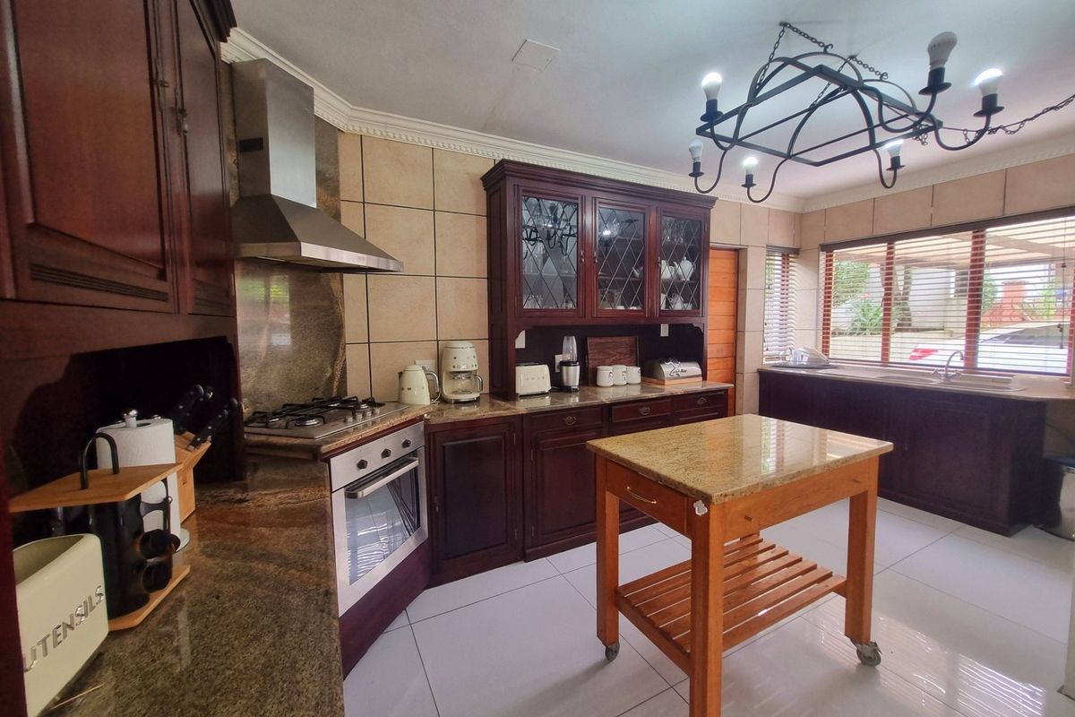 A well-appointed kitchen featuring dark wood cabinetry, granite countertops, a gas hob with extractor, and tiled flooring, offering a classic and functional workspace.