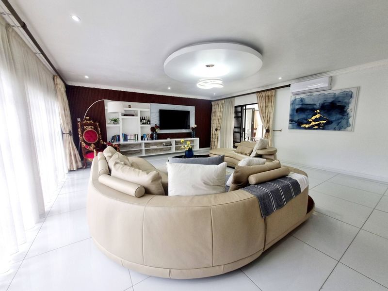 Spacious living room featuring tiled flooring, a built-in media wall, recessed ceiling lighting, and split-system air conditioning, with large sliding doors providing natural light.