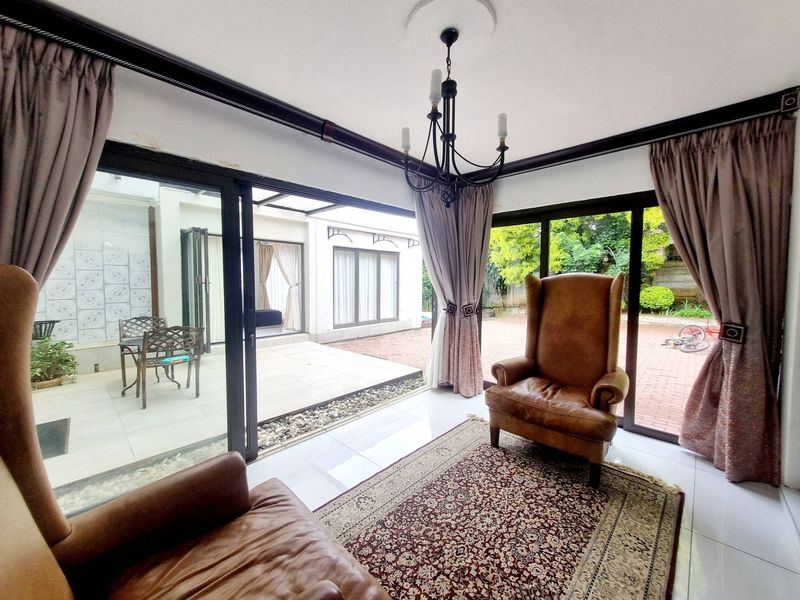 Bright living room featuring large sliding glass doors that open onto a paved patio area, complemented by tiled flooring and a classic chandelier.