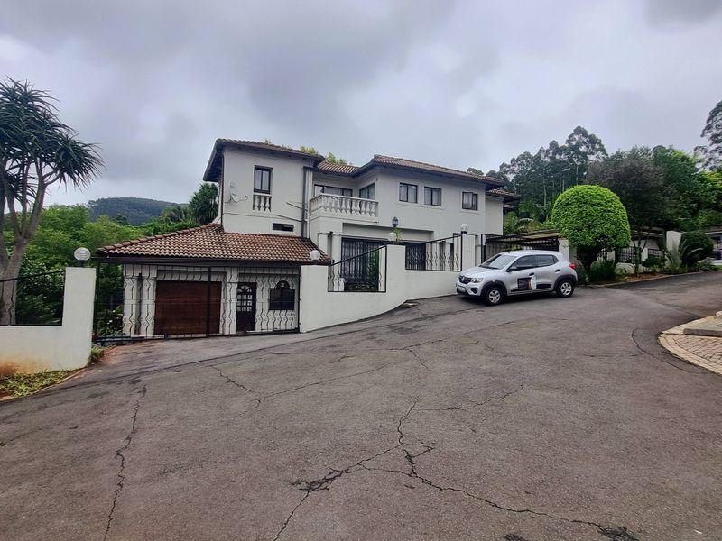 Front elevation of a multi-story residential house featuring a tiled roof, balcony, and paved driveway with a secure garage entrance.