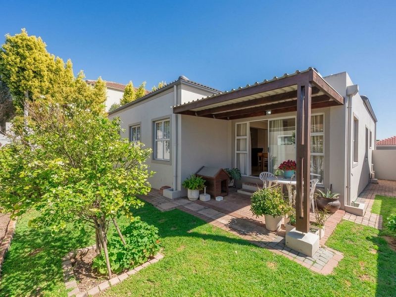 Rear view of the property featuring a covered timber pergola patio, paved outdoor area, and a well-maintained garden.