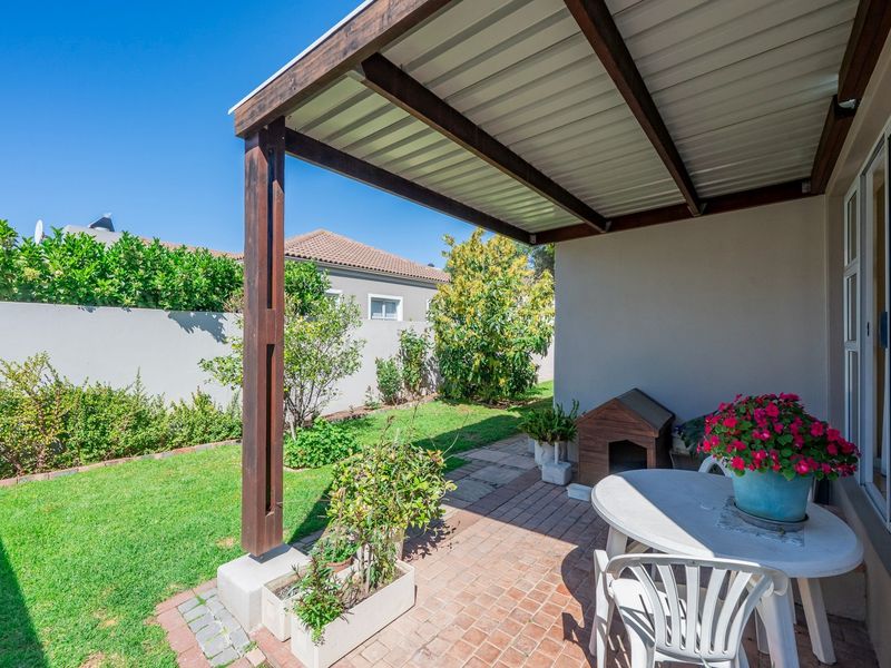A covered patio area featuring brick paving and timber support posts, providing direct access to the garden through a sliding glass door.