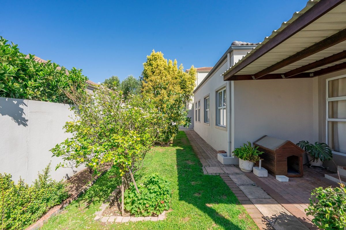 A side garden area featuring a paved walkway, a covered patio section, and a boundary wall, providing a clean and well-maintained outdoor space.