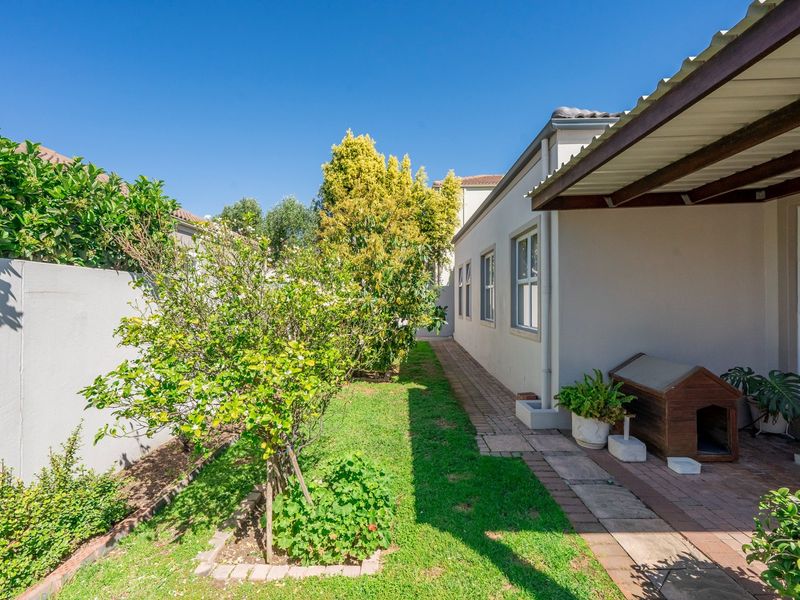 A side garden area featuring a paved walkway, a covered patio section, and a boundary wall, providing a clean and well-maintained outdoor space.