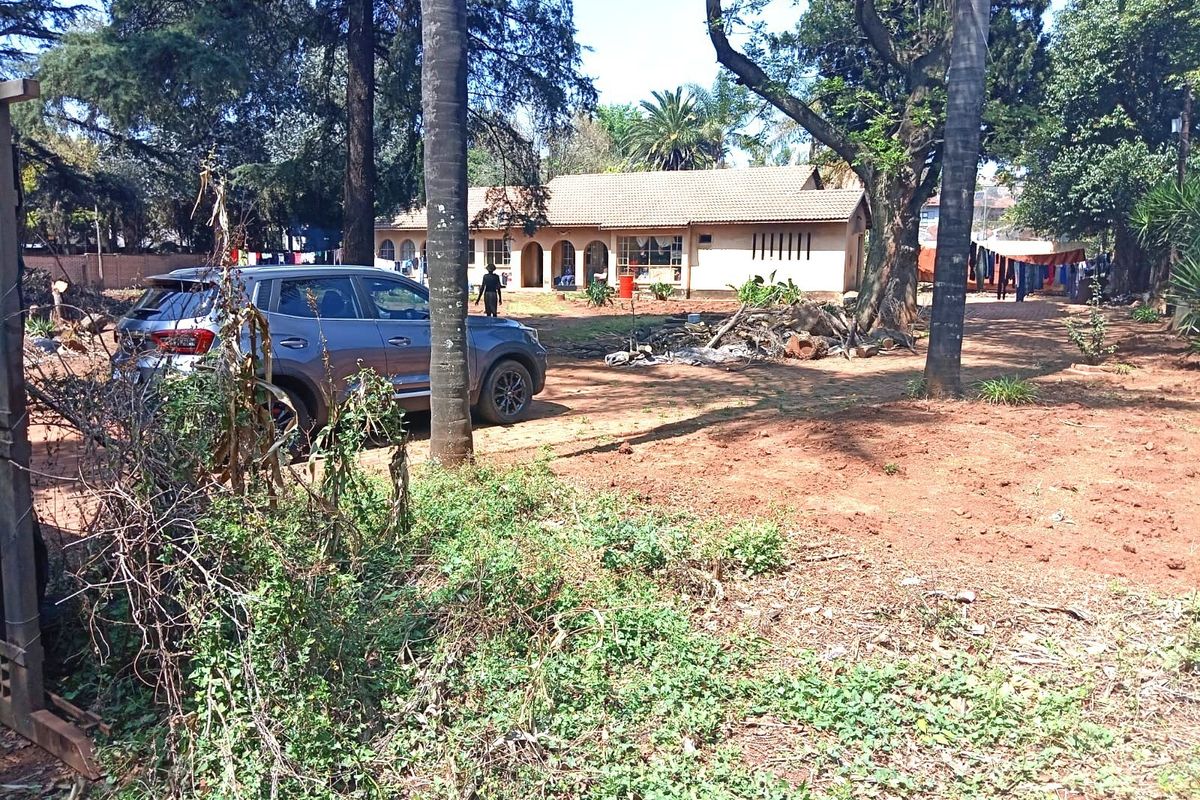 A view of the rear exterior of the house featuring a tiled roof and an arched veranda, set within a large, unmaintained garden area.