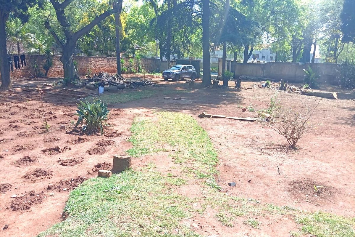 A large, expansive garden area featuring mature trees and a perimeter brick wall, currently requiring landscaping and maintenance to reach its full potential.