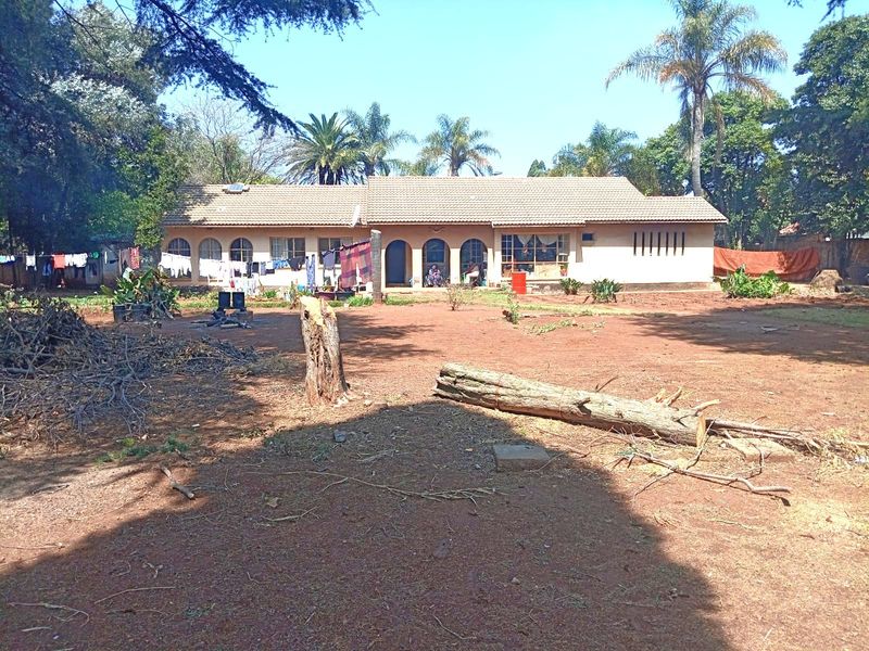 Rear view of a single-story house featuring a tiled roof and arched architectural details, set within a large, unlandscaped garden area.