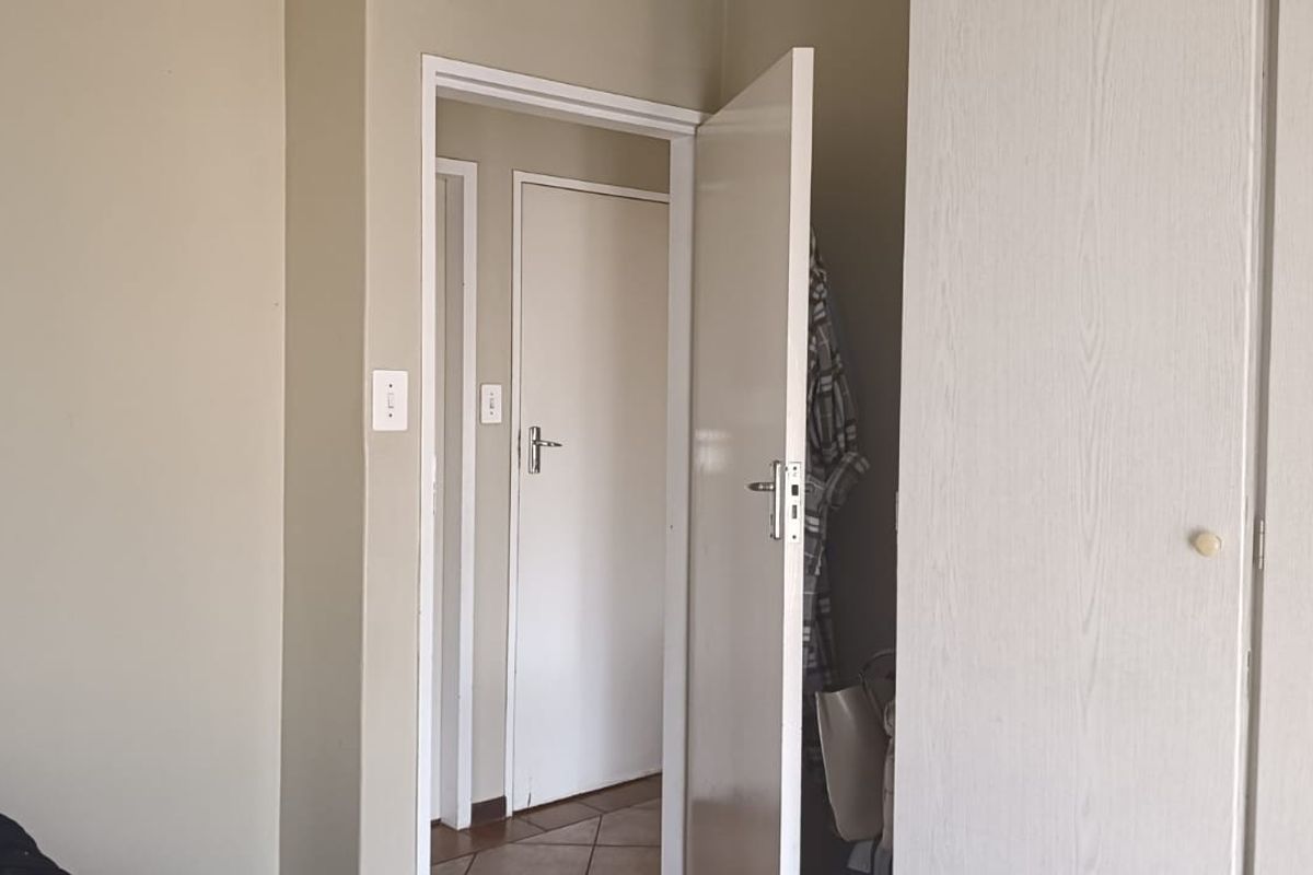 A bedroom interior featuring built-in wardrobe cabinetry and access to an adjoining hallway with tiled flooring.