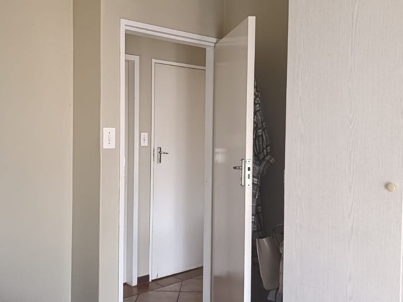 A bedroom interior featuring built-in wardrobe cabinetry and access to an adjoining hallway with tiled flooring.