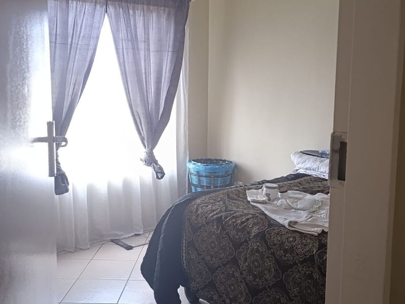 A bedroom featuring tiled flooring and a window with curtains, viewed from the doorway.