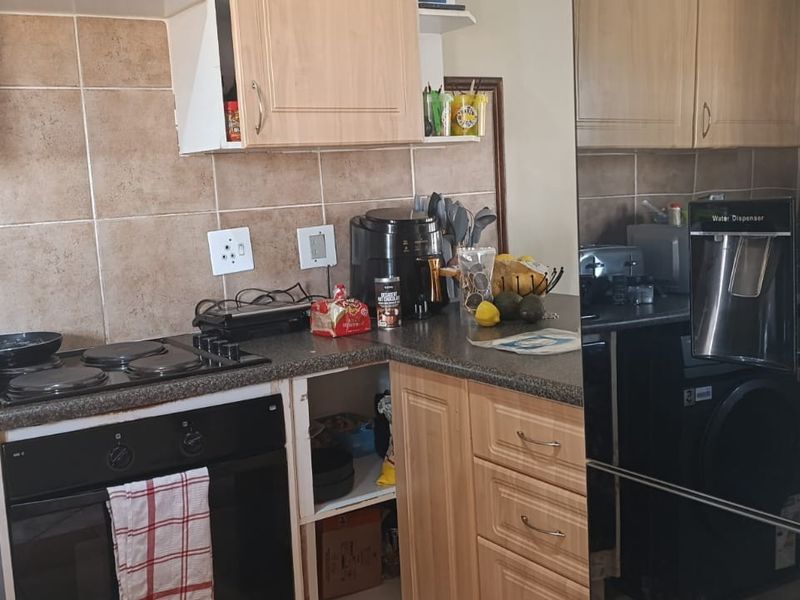 A compact kitchen featuring laminate cabinetry, tiled splashbacks, and built-in cooking appliances, currently showing signs of wear and a missing cabinet door.
