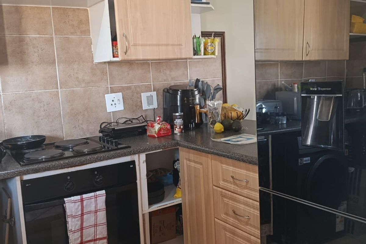 A compact kitchen featuring laminate cabinetry, tiled splashbacks, and built-in cooking appliances, currently showing signs of wear and a missing cabinet door.