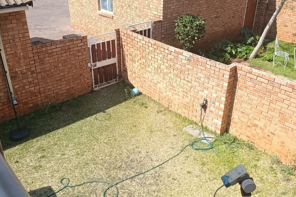 A private rear garden area featuring a brick boundary wall, a pedestrian gate, and a small lawn with an outdoor water tap.