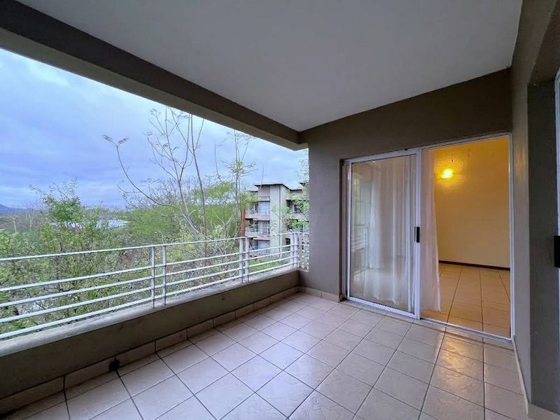 A covered balcony featuring tiled flooring, a metal balustrade, and a sliding glass door providing access to the interior living space.