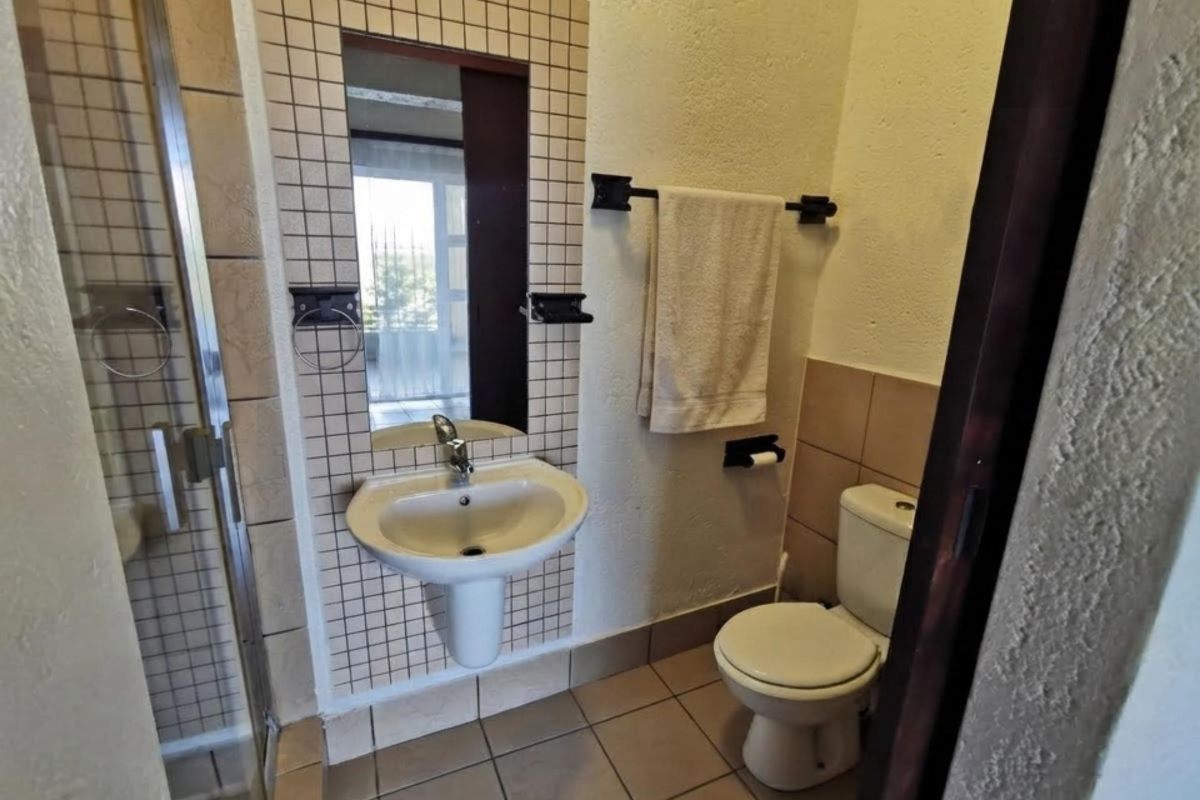 Compact bathroom featuring a pedestal washbasin, tiled splashback, shower enclosure, and toilet with neutral floor tiling.