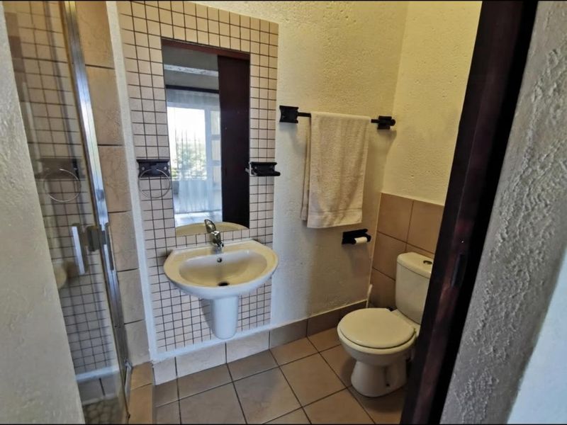 Compact bathroom featuring a pedestal washbasin, tiled splashback, shower enclosure, and toilet with neutral floor tiling.