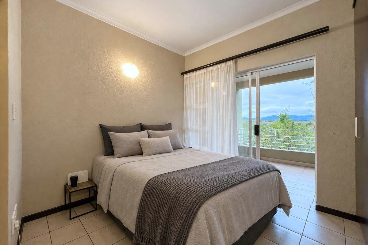A well-maintained bedroom featuring tiled flooring, a built-in cupboard, and a sliding glass door providing direct access to a private balcony with scenic views.