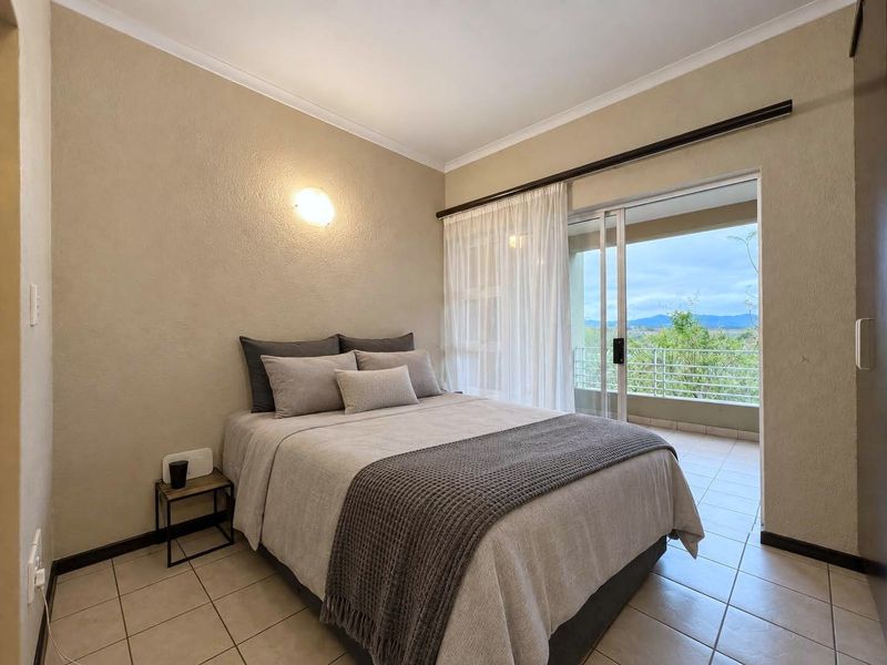 A well-maintained bedroom featuring tiled flooring, a built-in cupboard, and a sliding glass door providing direct access to a private balcony with scenic views.