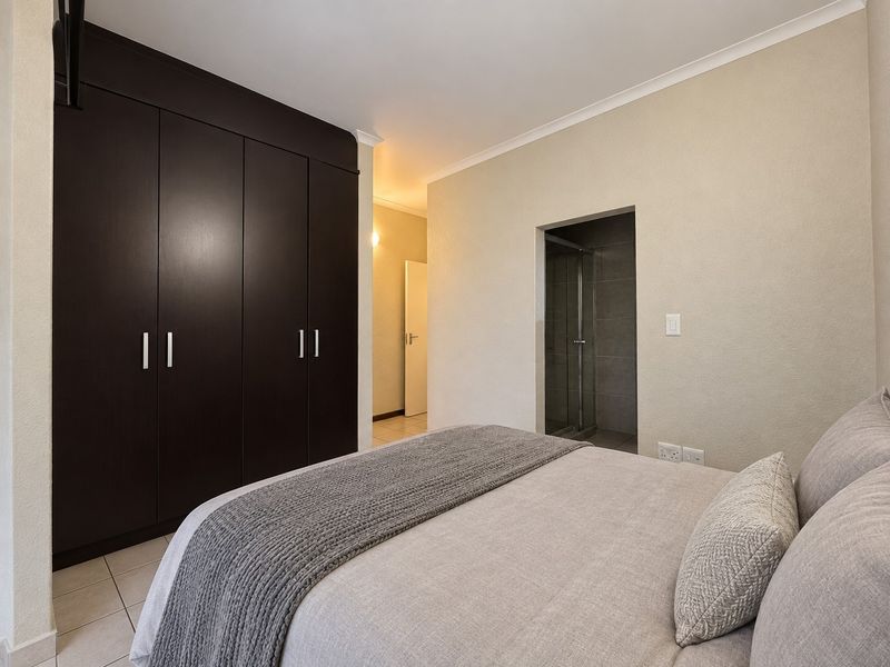 A well-maintained bedroom featuring dark built-in cupboards, tiled flooring, and direct access to an en-suite shower room.