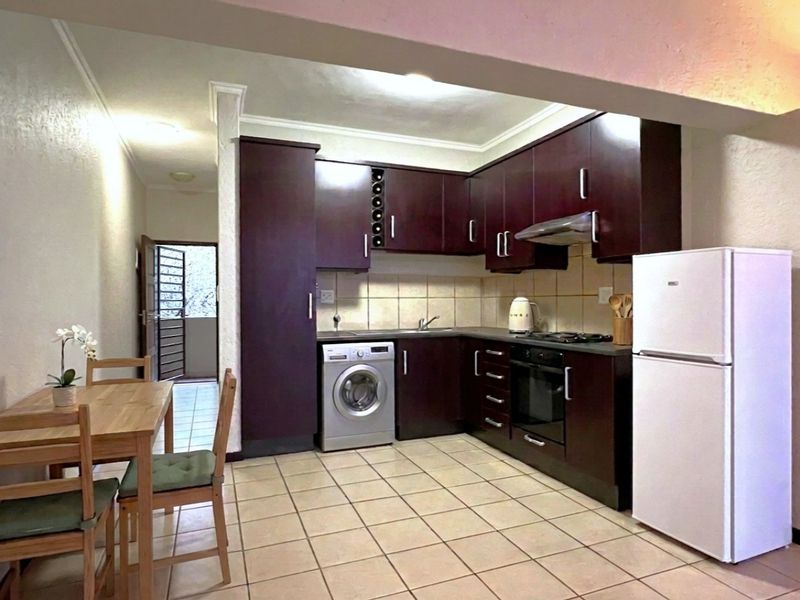 Open-plan kitchen featuring dark wood cabinetry, tiled flooring, built-in oven, gas hob, and integrated laundry plumbing, flowing into a dining area.