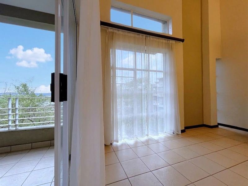 Spacious living area featuring high ceilings, tiled flooring, and large sliding glass doors providing direct access to a private balcony with scenic views.