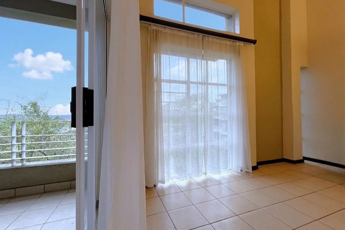 Spacious living area featuring high ceilings, tiled flooring, and large sliding glass doors providing direct access to a private balcony with scenic views.
