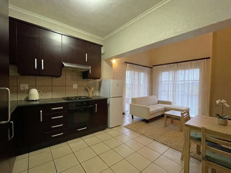 Open-plan kitchen and living area featuring dark wood cabinetry, built-in oven, gas hob, and tiled flooring with direct access to the patio.