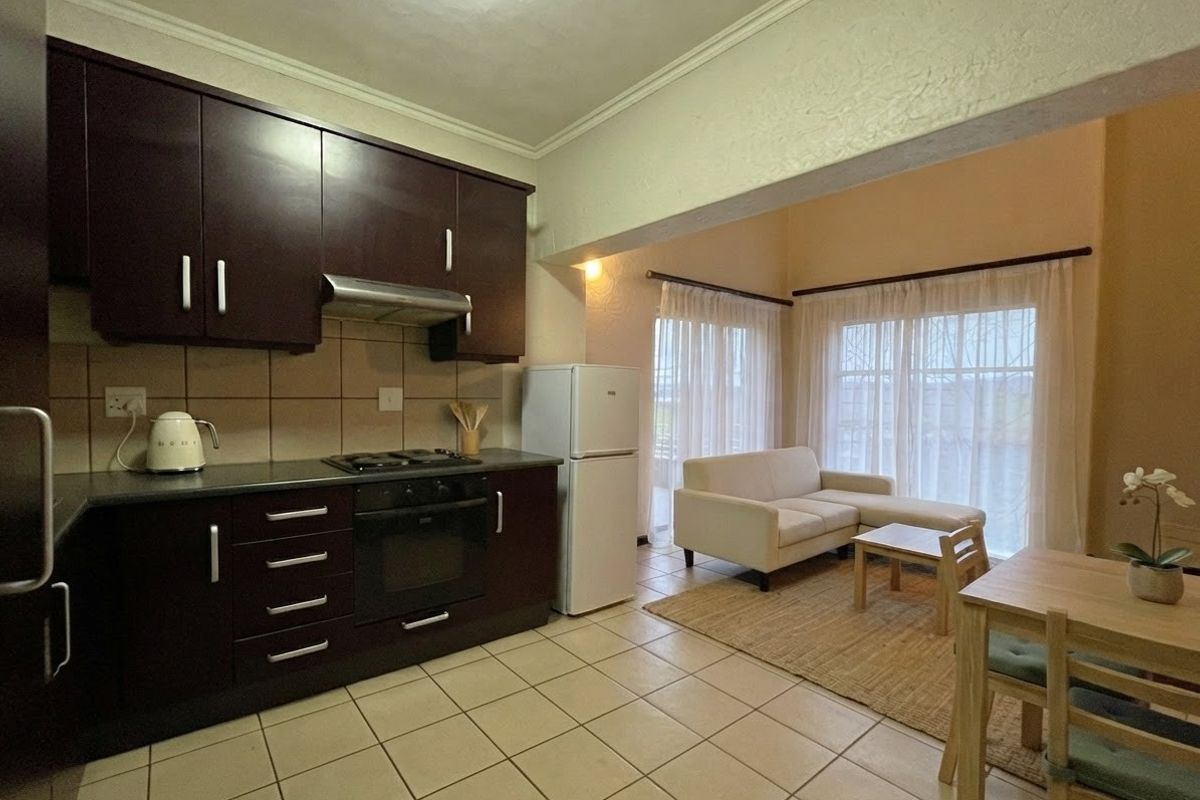 Open-plan kitchen and living area featuring dark wood cabinetry, built-in oven, gas hob, and tiled flooring with direct access to the patio.