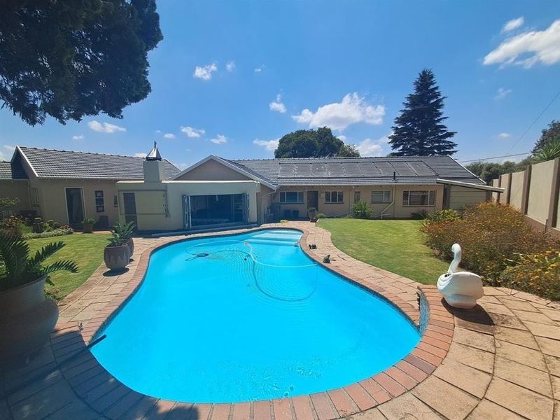 A well-maintained backyard featuring a swimming pool with solar heating panels, surrounded by a landscaped garden and brick-paved patio area.