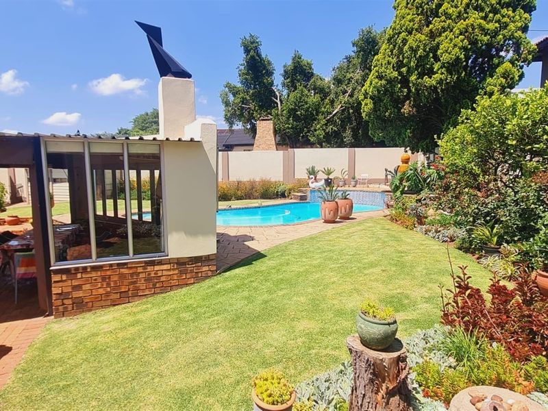 A well-maintained outdoor entertainment area featuring a swimming pool, paved patio, and a built-in outdoor fireplace set within a landscaped garden.