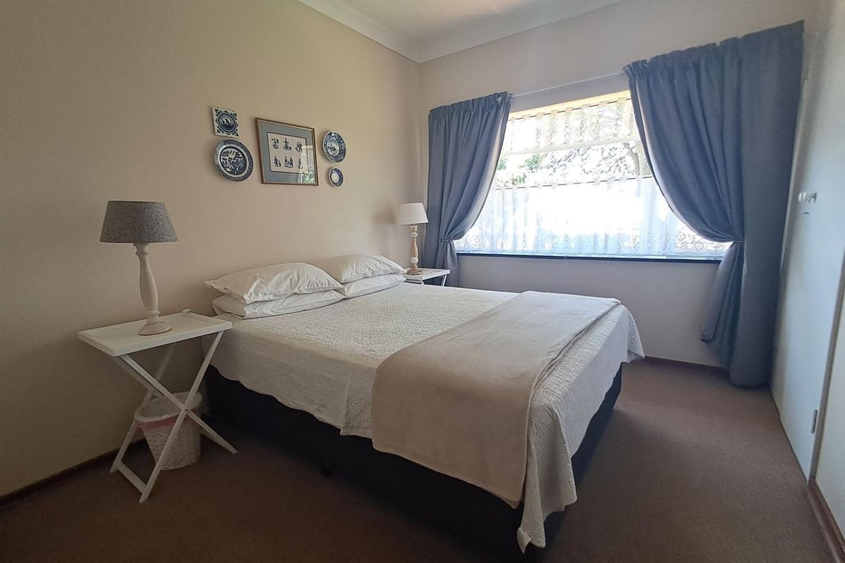 A well-maintained bedroom featuring neutral wall tones, carpeted flooring, and a large window with curtain fixtures.