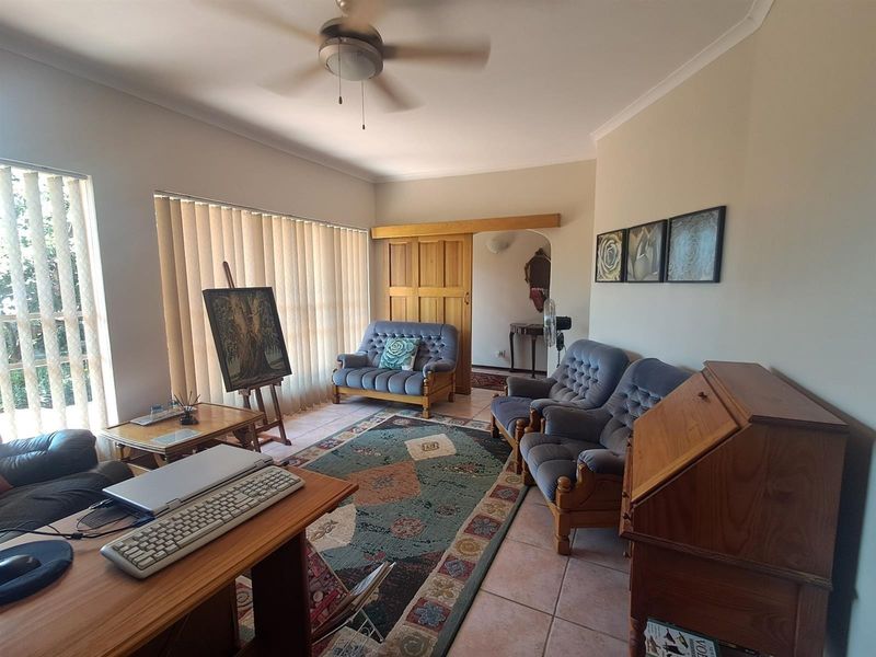 A living room featuring tiled flooring, a ceiling fan, and vertical blinds, providing a functional space with a sliding wooden door entry.