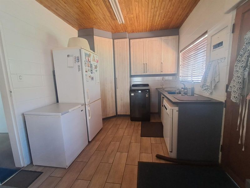 Functional laundry room featuring built-in cabinetry, laminate countertops, a stainless steel sink, and timber ceiling finishes.