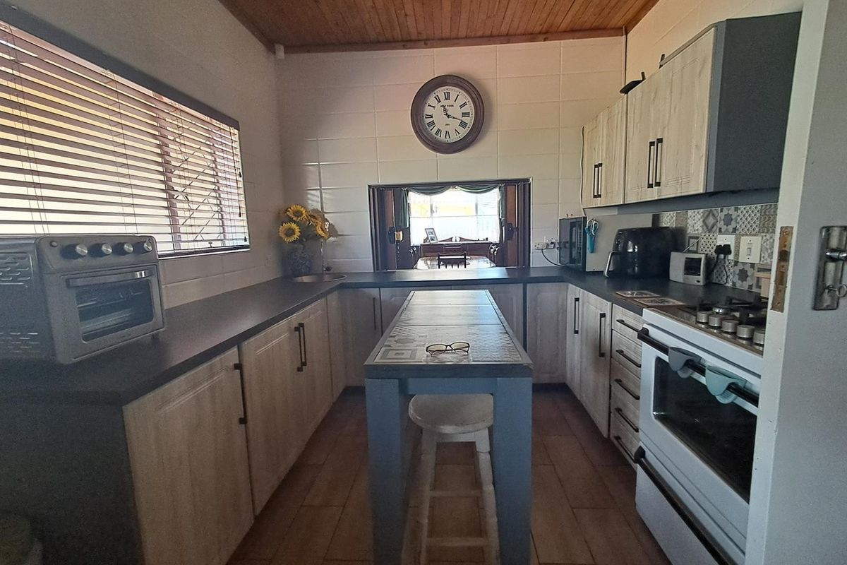 A functional kitchen featuring timber ceilings, tiled flooring, built-in cabinetry, and a central island, with a pass-through window connecting to the adjacent living area.