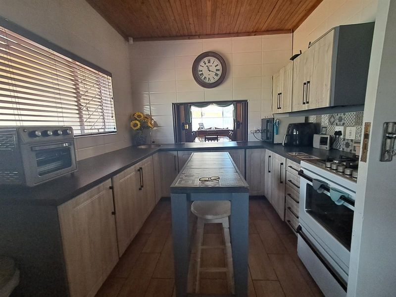 A functional kitchen featuring timber ceilings, tiled flooring, built-in cabinetry, and a central island, with a pass-through window connecting to the adjacent living area.