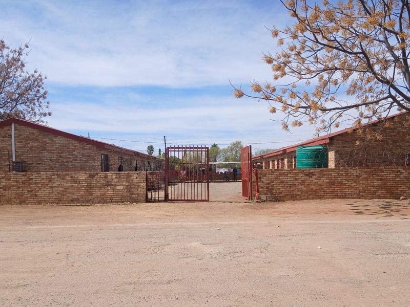 Front view of a face brick residential property featuring a gated entrance, perimeter walling, and an integrated water storage tank.