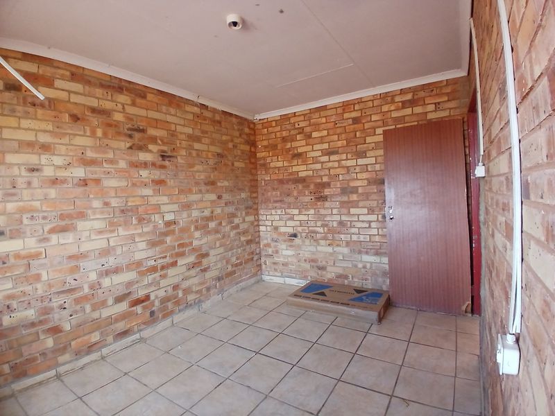 An empty bedroom featuring exposed brick walls, ceramic floor tiles, and surface-mounted electrical conduits, presenting a blank canvas for renovation.