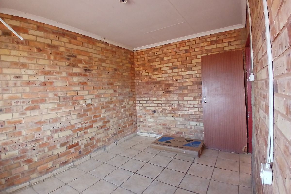 An empty bedroom featuring exposed brick walls, ceramic floor tiles, and surface-mounted electrical conduits, presenting a blank canvas for renovation.