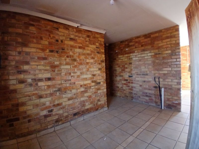 An unfinished utility or laundry space featuring exposed brick walls, ceramic floor tiling, and visible plumbing connections ready for installation.