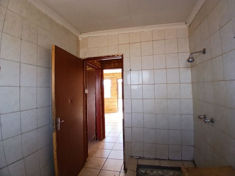 A basic, empty bathroom featuring tiled walls and flooring with a wall-mounted shower fixture, requiring cosmetic updates to modernize the space.