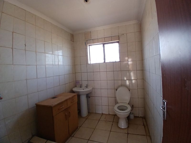 A functional bathroom featuring a pedestal washbasin, toilet, and built-in vanity cabinet, finished with full-height wall tiling and floor tiles.