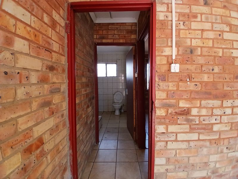 A hallway with exposed brick walls and tiled flooring leading to a bathroom with a toilet.