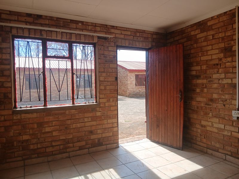 An empty living area featuring exposed brick walls, tiled flooring, and a timber door leading to an exterior courtyard.