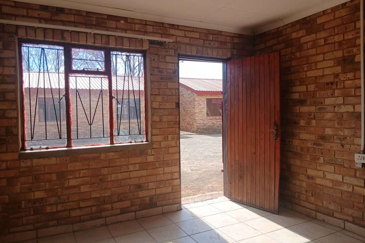 An empty living area featuring exposed brick walls, tiled flooring, and a timber door leading to an exterior courtyard.