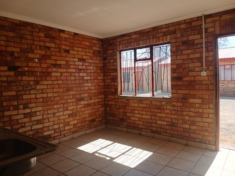 An empty kitchen area featuring exposed brick walls, tiled flooring, and a stainless steel sink, offering a blank canvas for renovation.