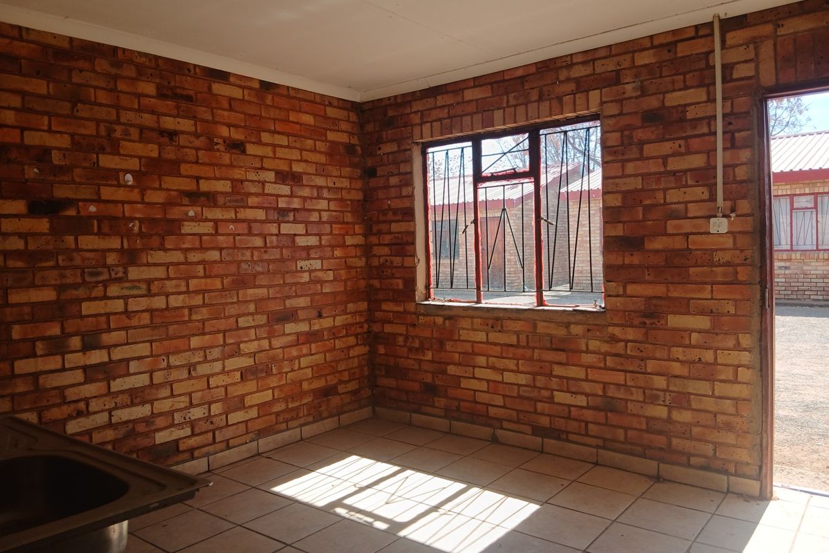 An empty kitchen area featuring exposed brick walls, tiled flooring, and a stainless steel sink, offering a blank canvas for renovation.