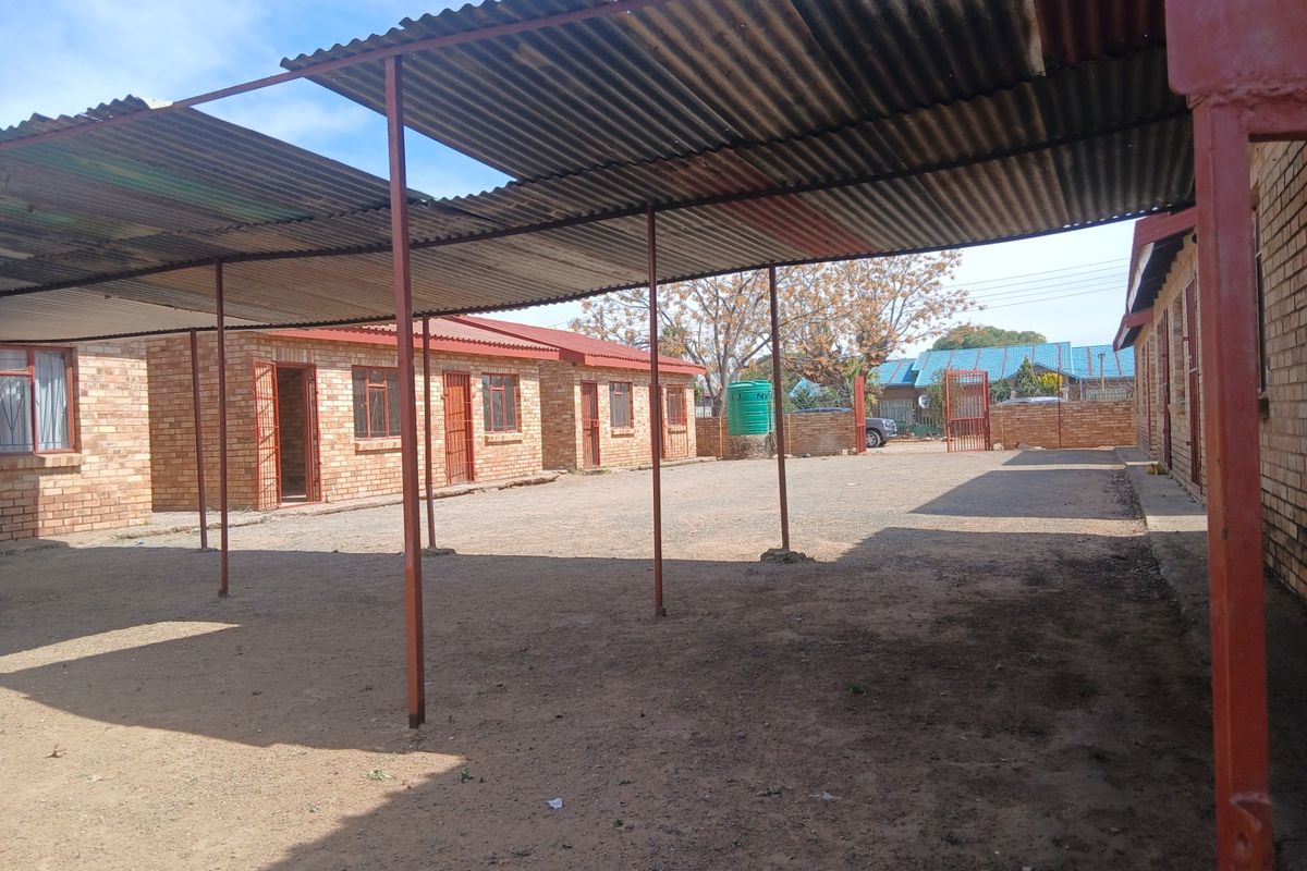 A large, open rear courtyard area featuring a long corrugated metal carport structure, exposed brick exterior walls, and a water storage tank.