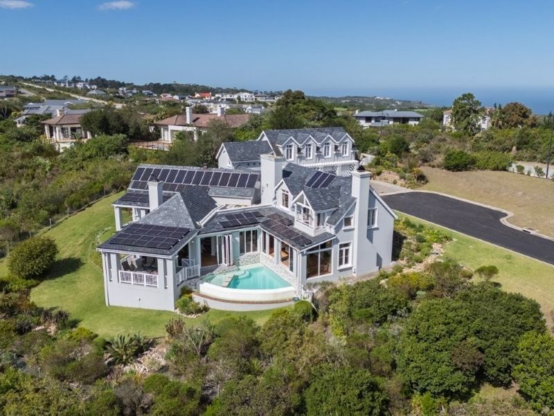 Aerial view of a large residential property featuring a slate roof with integrated solar panels, a swimming pool, and landscaped grounds in a coastal setting.
