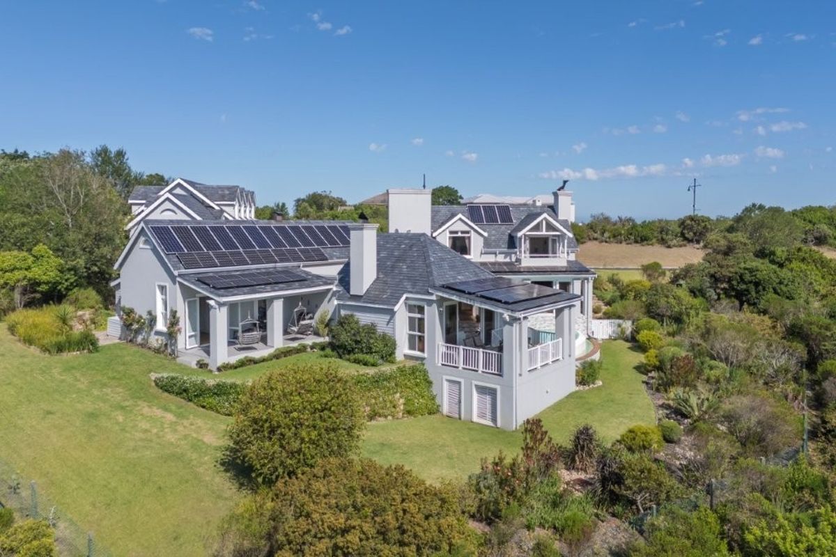 Aerial view of a large residential property featuring a slate roof, extensive solar panel installation, and well-maintained landscaped gardens with covered patio areas.