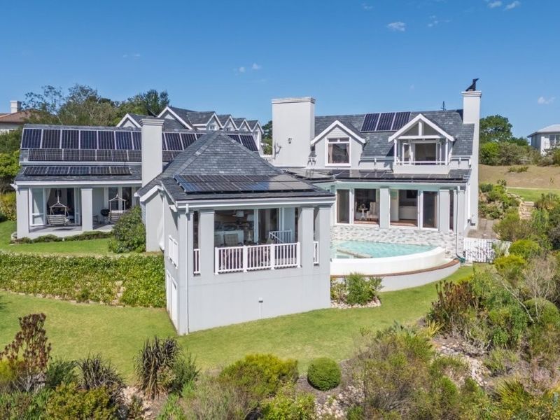 Aerial view of a large residential property featuring a swimming pool, extensive solar panel installation, and landscaped gardens.